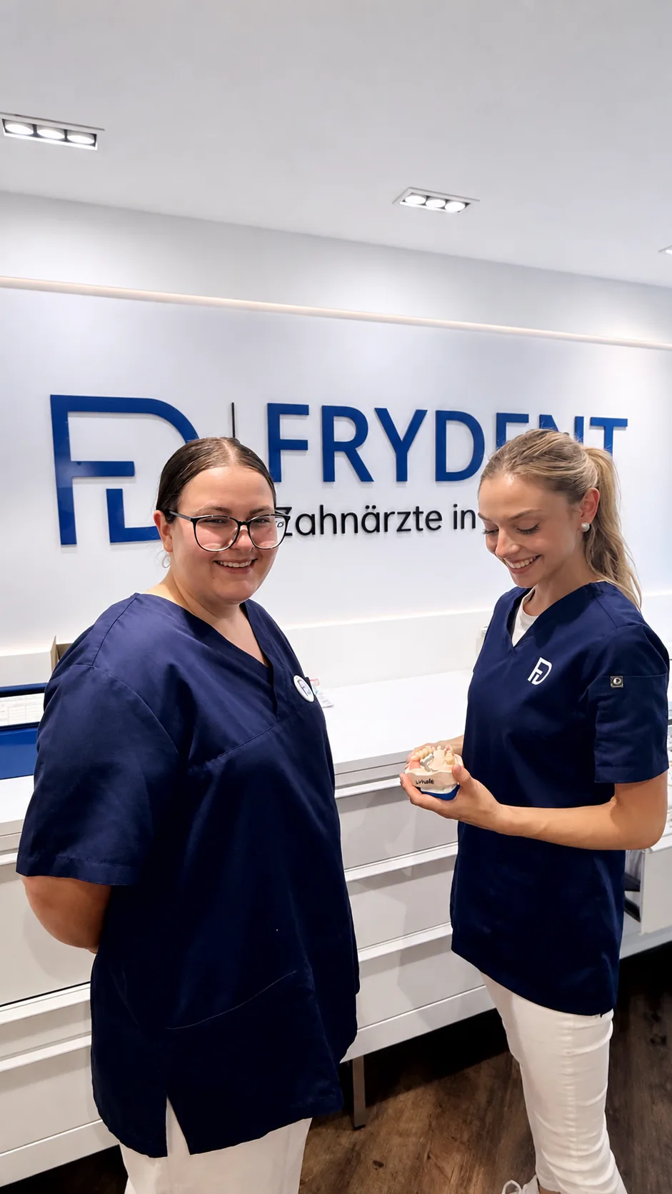 Kiara und Kollegin mit einem Zahnmodell vor dem FRYDENT-Logo